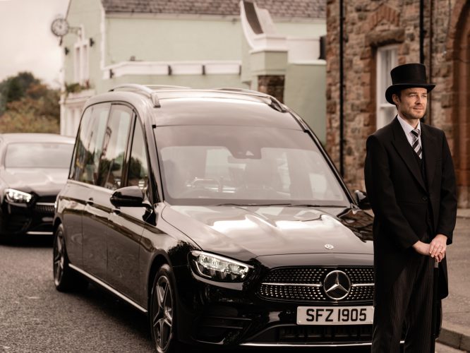 Man in top hat and suit infront of a funeral car