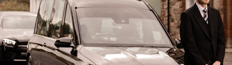 Man in top hat and suit infront of a funeral car